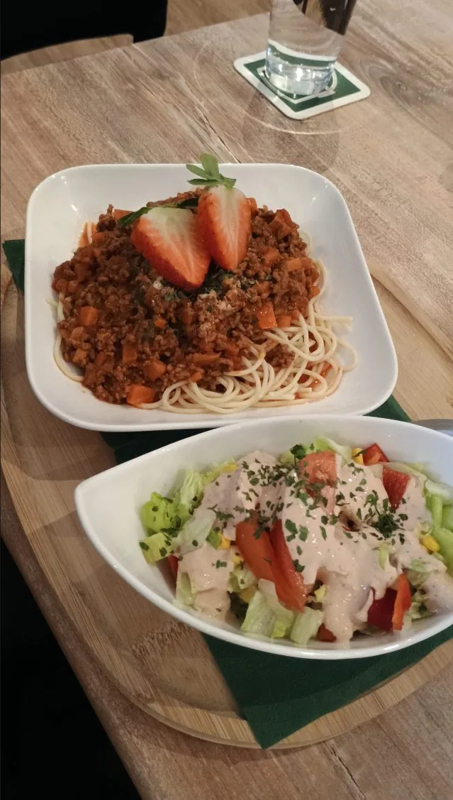 Spaghetti Bolognese mit Salatbeilage am Tisch serviert
